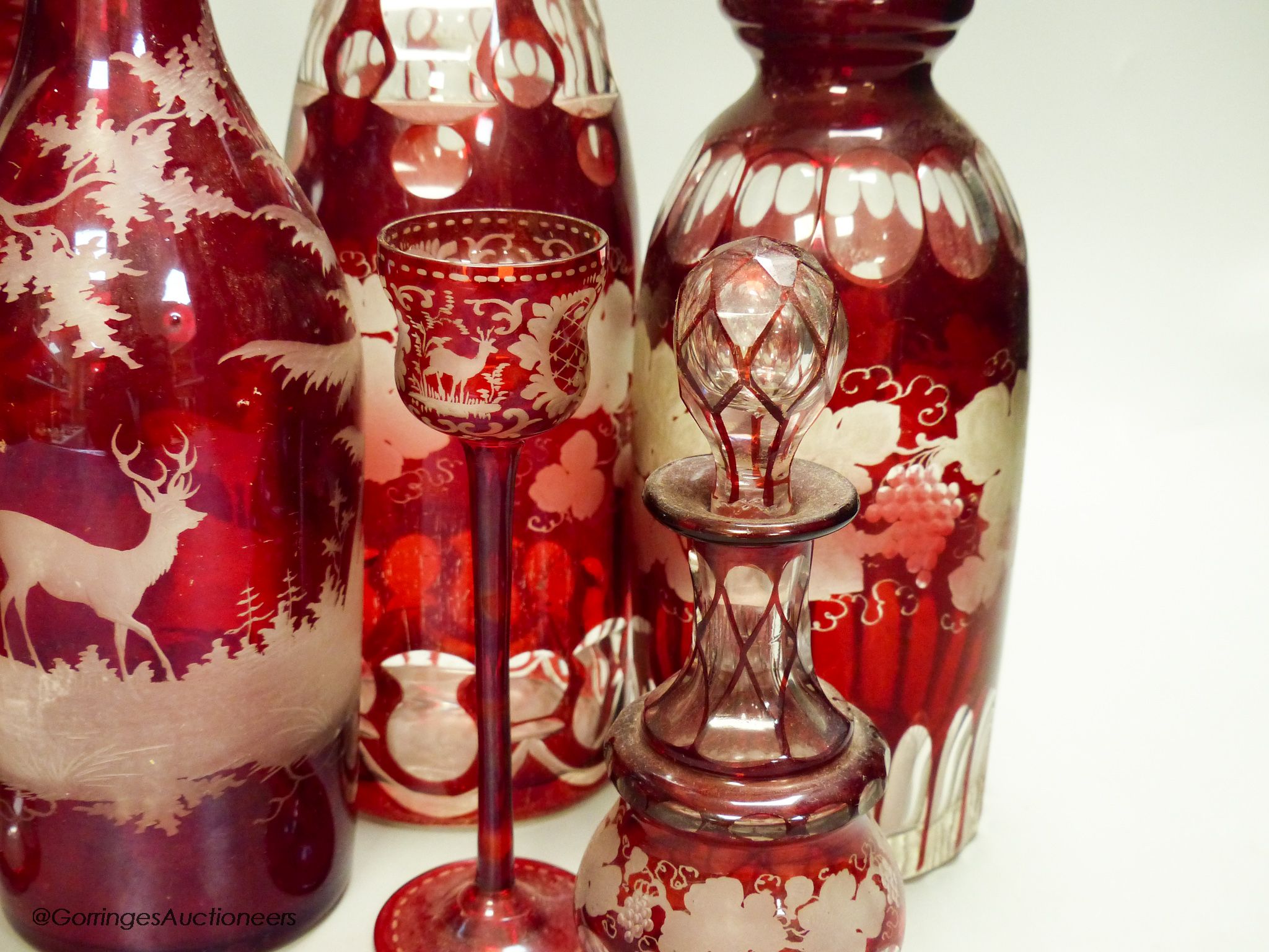 A collection of six Bohemian ruby flashed wheel engraved glass decanters, tallest 40cm, a similar spa beaker and liqueur glass